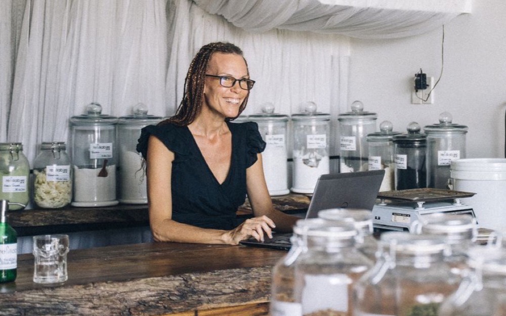 Una emprendedora sonríe mientras trabaja con su notebook en el mostrador de su tienda